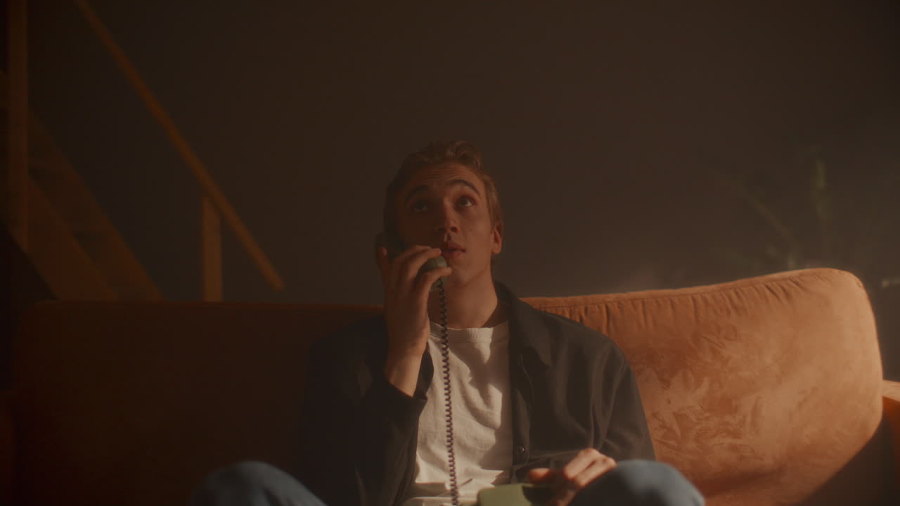 Young Man Sitting on Sofa in Retro Room, Talking on Corded Phone