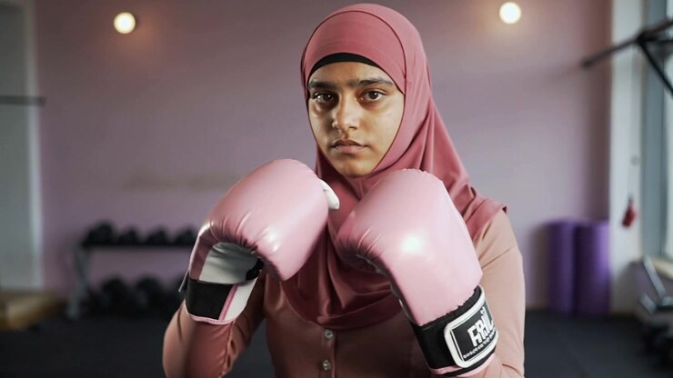 Inizio dell'esercizio di allenamento, donna con hijab che colpisce verso la telecamera in palestra, con guanti rosa