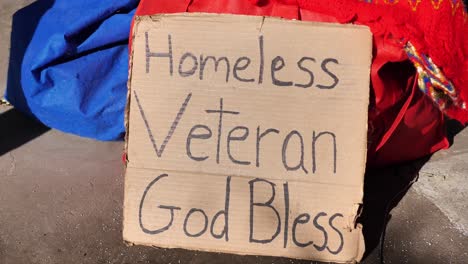 cardboard signs that read "homeless, anything helps" and "hungry and homeless" sitting on pile of stuff