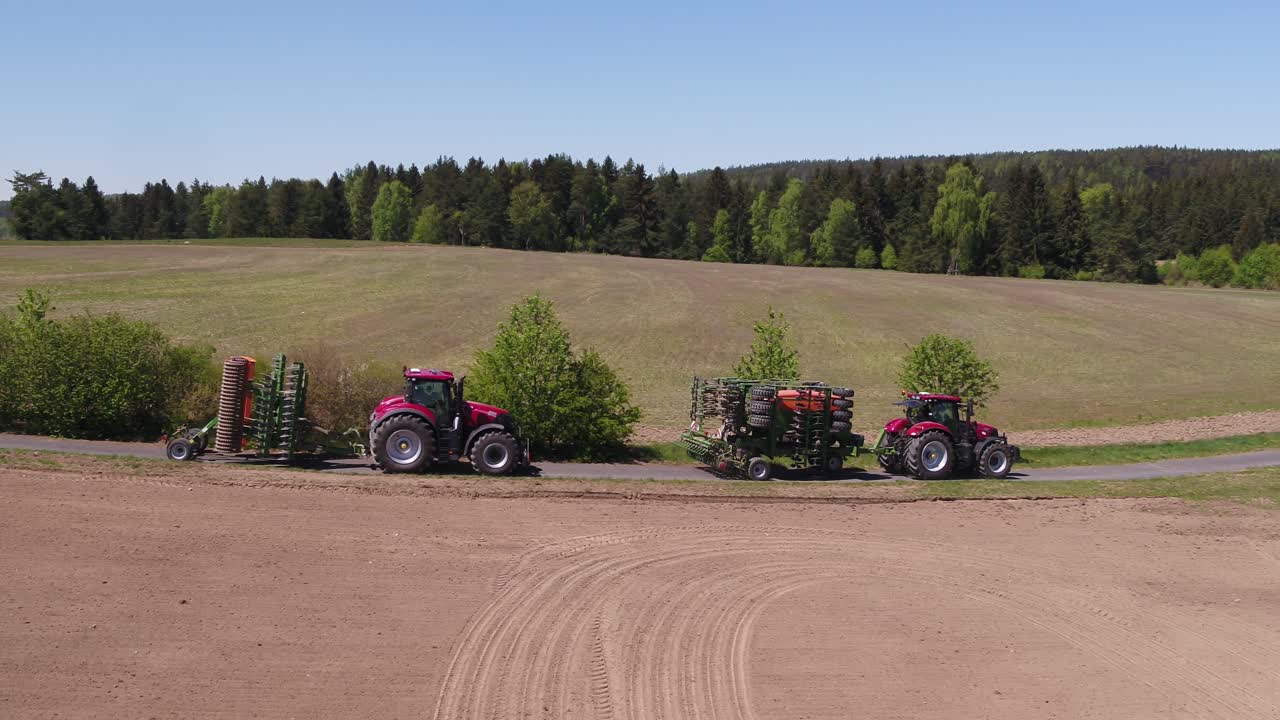 Tracking shot of two agricultural vehicles towing folded machines through rural road in spring landscape