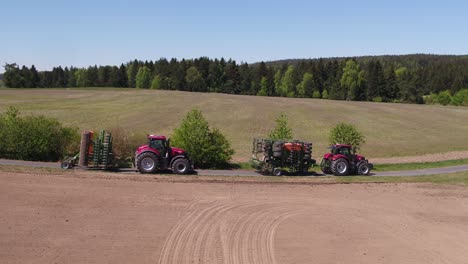 tracking shot of two agricultural vehicles towing folded machines through rural road in spring landscape