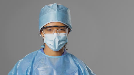 retrato de una cirujana sonriente con gafas de seguridad y máscara facial contra un fondo gris