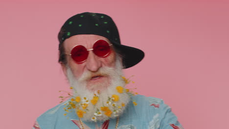 Close-up-cheerful-stylish-senior-flowered-beard-man-wearing-sunglasses,-charming-smile-on-pink-wall