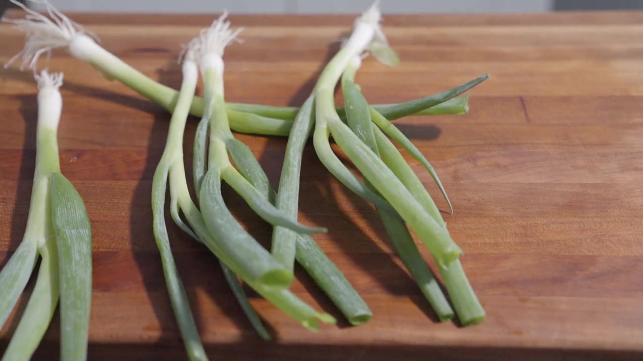 Een statische close-up opname van lente-uitjes die op een snijplank worden gegooid en verspreid. Perfect voor culinaire content, waarbij verse ingrediënten en de opwinding van voedselbereiding worden getoond.