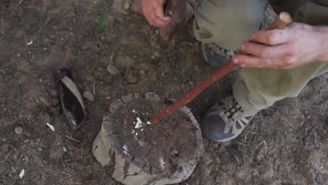 caucasian male survivalist sharpening stick with machete in wilderness