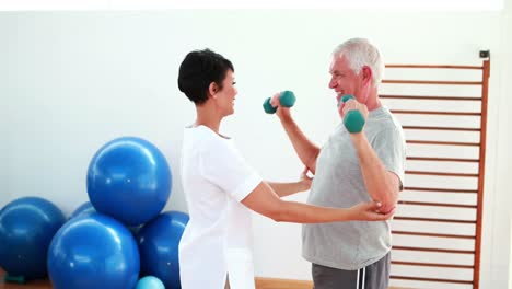 Hübsche-Physiotherapeutin-Hilft-älteren-Patienten-Beim-Heben-Von-Handgewichten