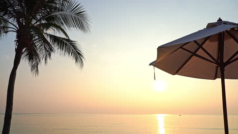 Tropical-Sunset-Above-Sea-Horizon,-Palm-Tree-and-Parasol,-Pristine-Vacation-Scenery