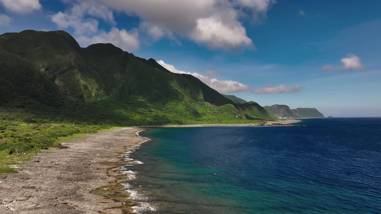 Tomada cinematográfica de drone da costa da Ilha das Orquídeas com montanhas verdes e oceano azul em um dia ensolarado.