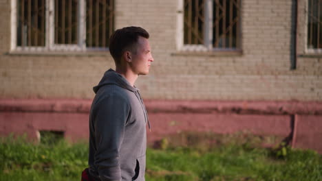 young person in light gray hoodie looking thoughtful, in profile against aged building with green grass. captures calm, introspective mood, perfect for themes of reflection