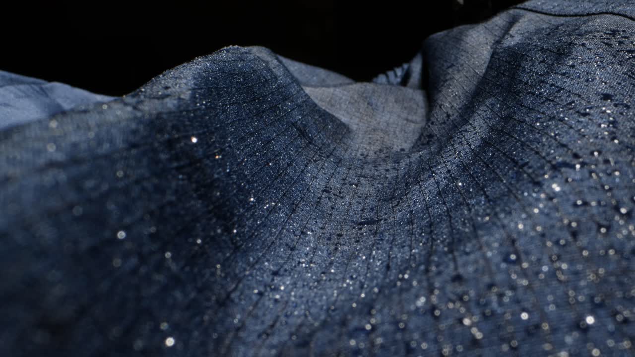 Waterproof clothing for tourism. Blue cloth texture with water drop close-up macro. Repellent waterproof breathable fabrics. Innovation waterproofing material test. High quality 4k footage