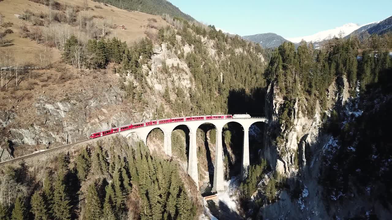 Drone footage of the Red Train Express passing through the Landwasser Viaduct the six-arched curved railway (Landwasserviadukt) Graubünden, Switzerland.Rhätische Bahn