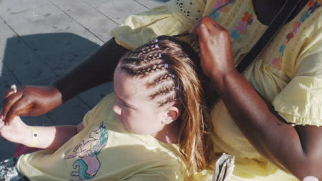 a young girl has her hair braided in plats on the street sidewalk-1