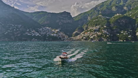 positano italy aerial v8 drone reverse flyover capturing a boat cruising in the sea bay with picturesque landscape of coastal cliffside village town in the backdrop - shot with mavic 3 cine - may 2023