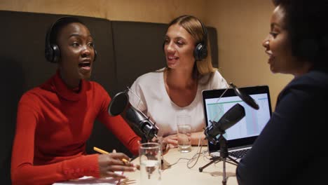 three diverse female radio hosts wearing headphones talking on microphone for radio podcast