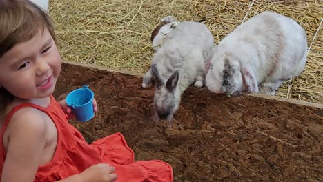 sonriendo feliz niña alimentando conejos con hojas verdes en una granja