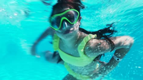 Happy-girl-in-goggles-swim-underwater-in-pool.-Close-up.