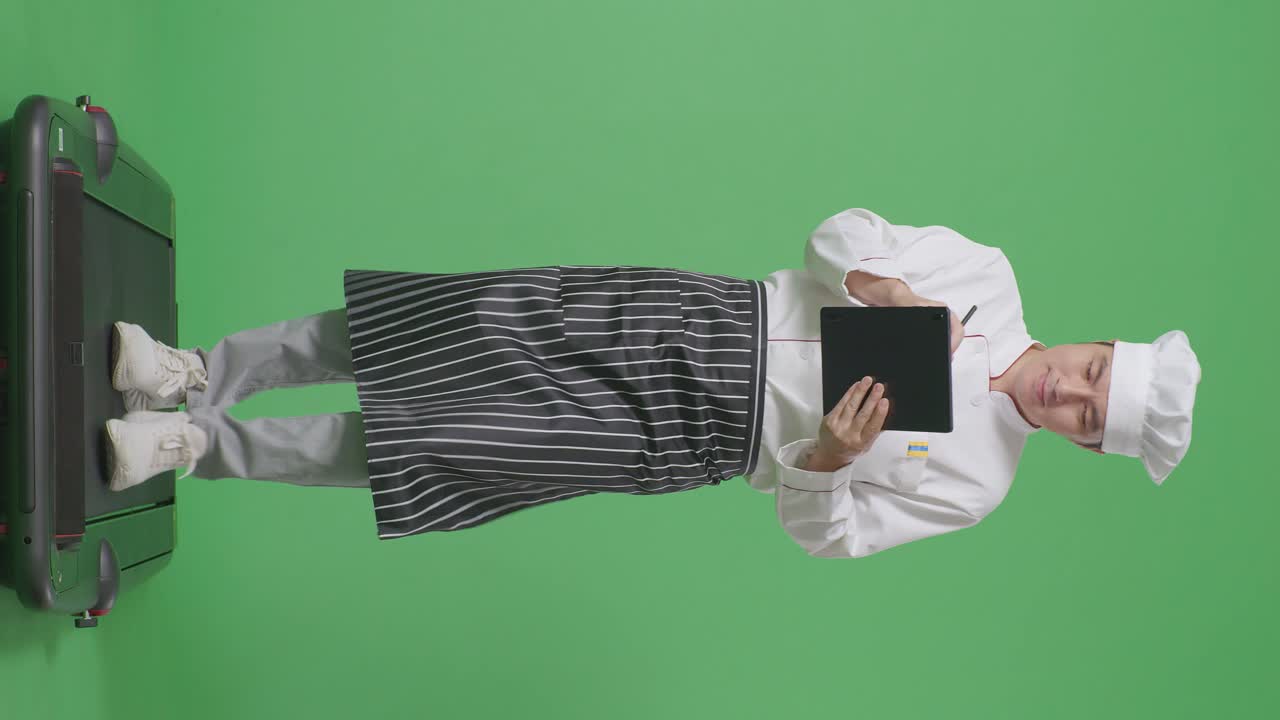 녹색 스크린 배경 스튜디오에서 트레드밀을 는 동안 태블릿에 메모를 취하는 아시아 남자 셰프의 전체 몸