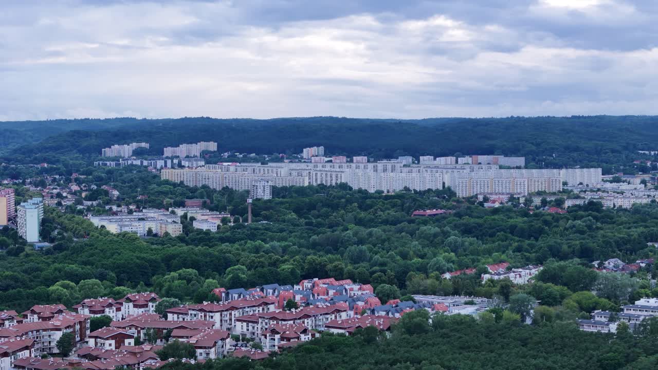 Aerial view of Gdansk, Poland, showcasing the Zaspa district with its large residential buildings, surrounded by lush green spaces and forests, under a cloudy sky, drone orbiting footage