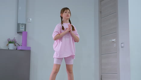 young child balancing on yellow rubber squat pads, extending hand forward for stability, background features gym equipment, including foam rollers and a storage cabinet