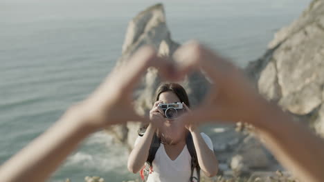 girl taking photo of two unrecognizable people doing heart gesture during hiking adventure