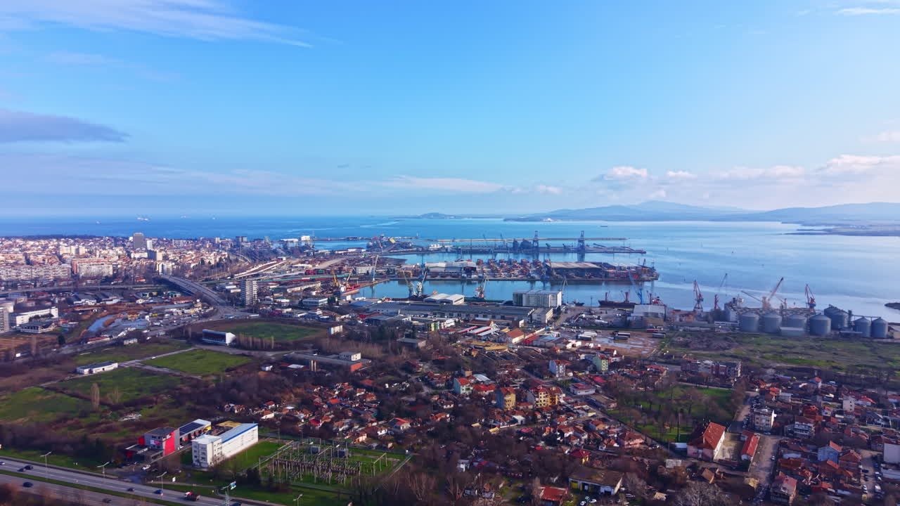 Area portuale con cantieri navali e paesaggio urbano visti dall'alto durante il giorno, con cielo sereno e colline distanti in vista.