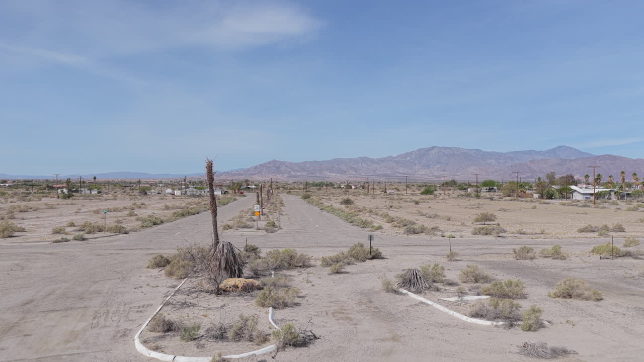 Ripresa con drone a bassa quota in volo in avanti sopra l'ex sito del Salton Bay Yacht Club a Salton City, California, verso Yacht Club Drive. Le montagne San Jacinto si ergono in lontananza