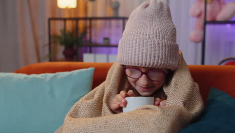 girl feeling sick and drinking warm drink on couch