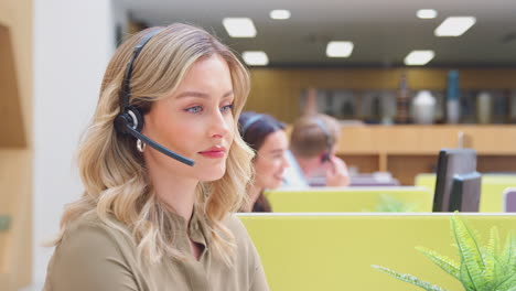 Portrait-Of-Businesswoman-Wearing-Phone-Headset-Working-At-Computer-In-Customer-Services-Centre