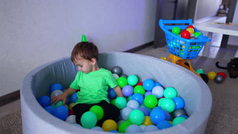 lovely adorable toddler playing in dry pool at home. happy kid lies smiling on the colorful balls. top view.
