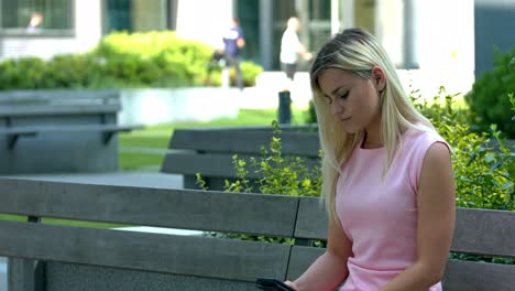 mujer joven sentada en un banco y enviando mensajes de texto en su teléfono celular