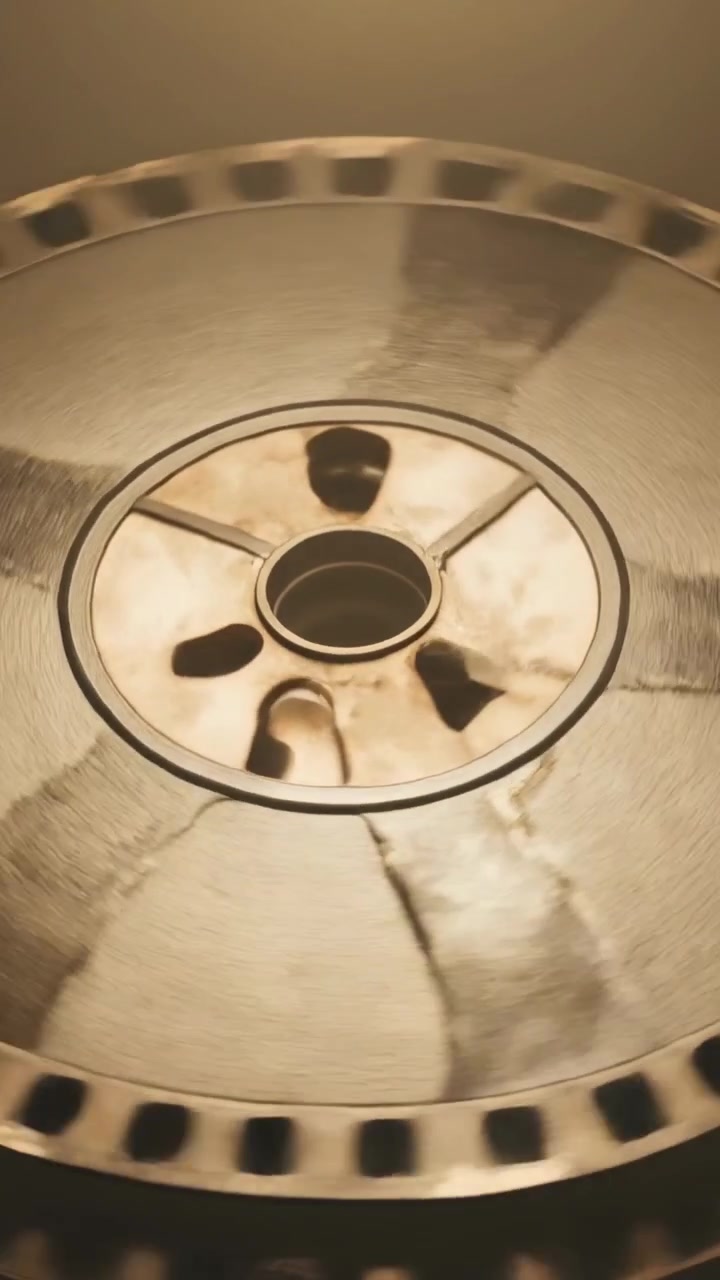 Vídeo vertical: Motor engrenando, carretel de metal girando lentamente em oficina escura, revelando fragmentos de cubo.