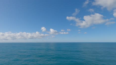 cumulus clouds appear motionless above a calm, deep-blue sea bathed in sunshine