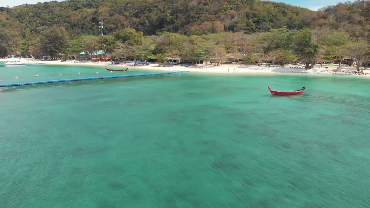 Idyllic Banana Beach Bay with floating dock platform and rural fishing boats moored on the emerald waters in Koh Hey , Thailand - Aerial ground level Fly-backwards shot