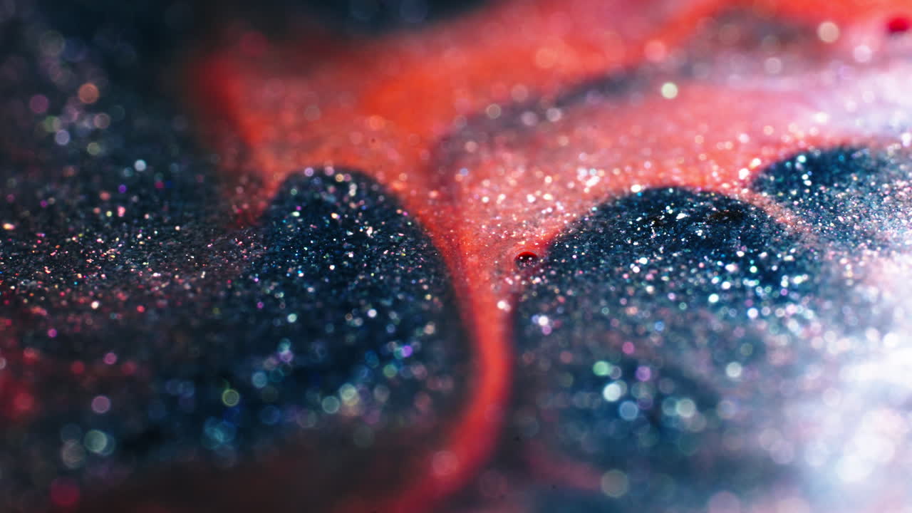 Colorful liquids mix with shimmering particles in a cosmic-like macro close-up shot