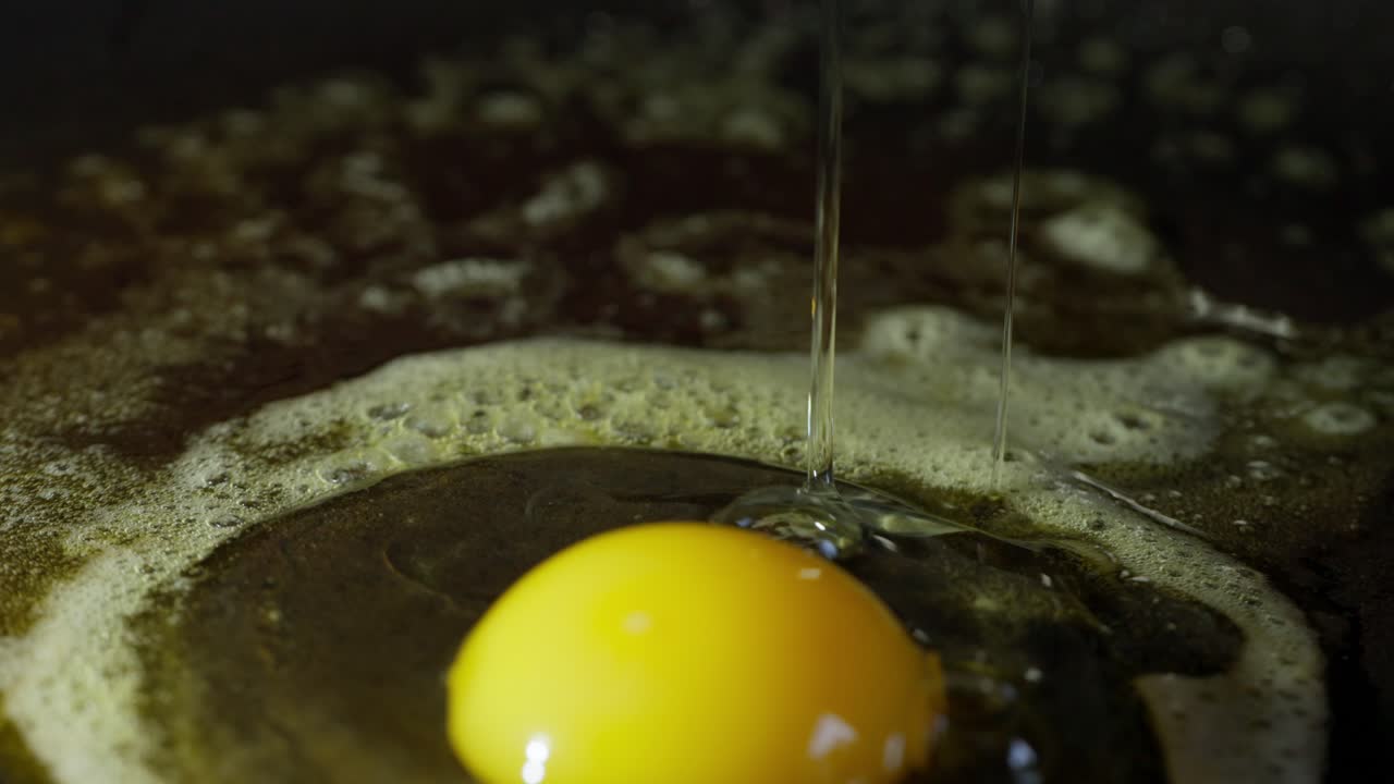 Slow-motion close-up of egg cracking and spreading into hot pan with bubbles, 4K