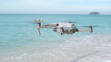 drone hovering on a beach with kayak and island in background