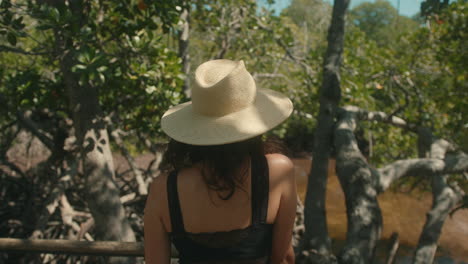 slow motion close-up of a caucasian woman with a straw hat on her back looking at a green forest