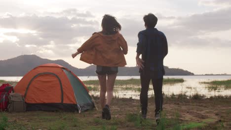 young asia campers couple run and raised arms at campsite near beach.