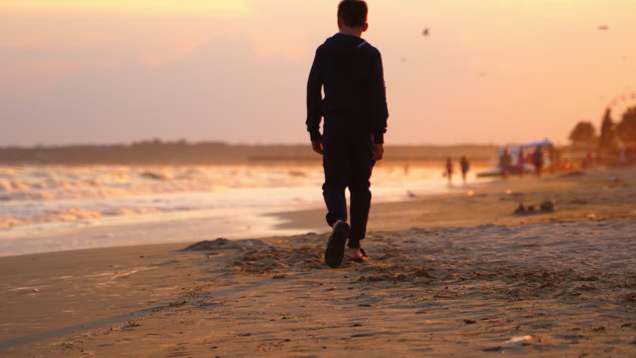 Boy walking at beach on sunset. Boy walking alone on the beach during sunset at seaside