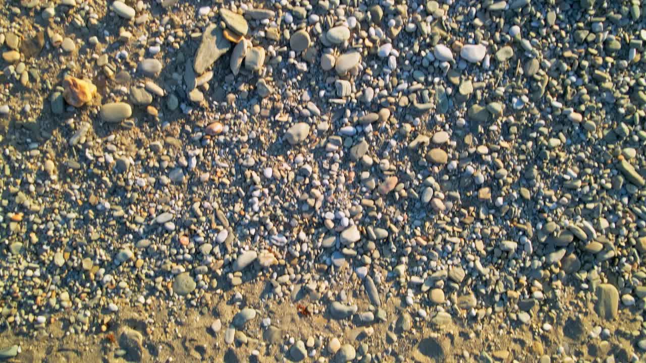Ripresa aerea con drone, dall'alto, dalla sabbia e dai ciottoli della spiaggia verso il mare limpido.