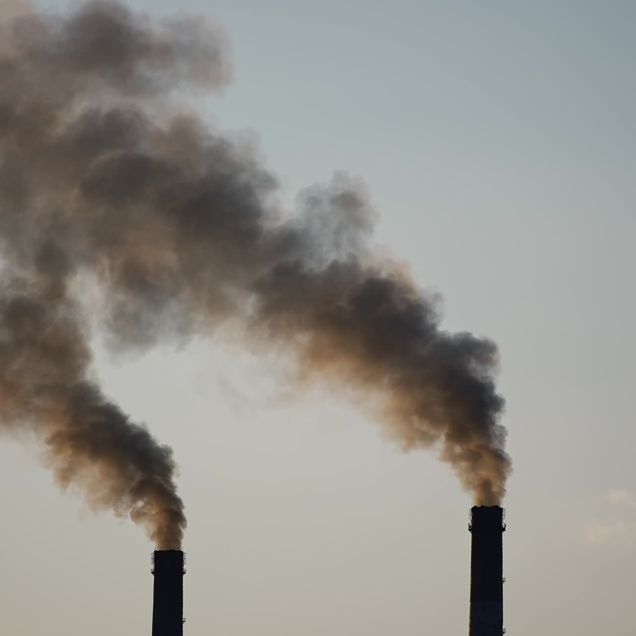 Tops of two plant chimneys polluting air with dark grey smoke. Environment pollution concept. Grey clear sky backdrop