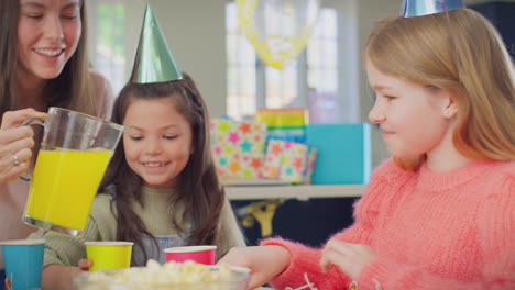 Mother-Pouring-Juice-Into-Cups-As-Children-Enjoy-Birthday-Party-At-Home