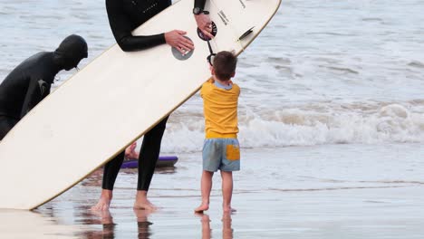 child interacts with surfboard by the sea