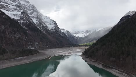 Luftaufnahme-Des-Klöntalersees-Mit-Einem-Reflektierenden-Türkisfarbenen-See,-Eingebettet-Zwischen-Schneebedeckten-Berggipfeln-Und-Steilen-Bewaldeten-Hängen