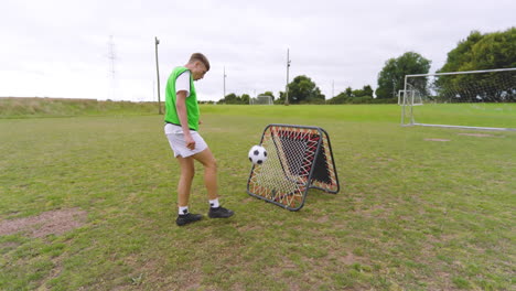 male soccer player training, warming up and bouncing ball with leg at net on pitch