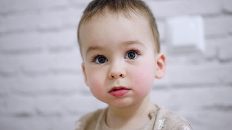 adorable big-eyed baby boy with mousy hair. portrait of a calm caucasian kid focused on something. close up. blurred white backdrop.