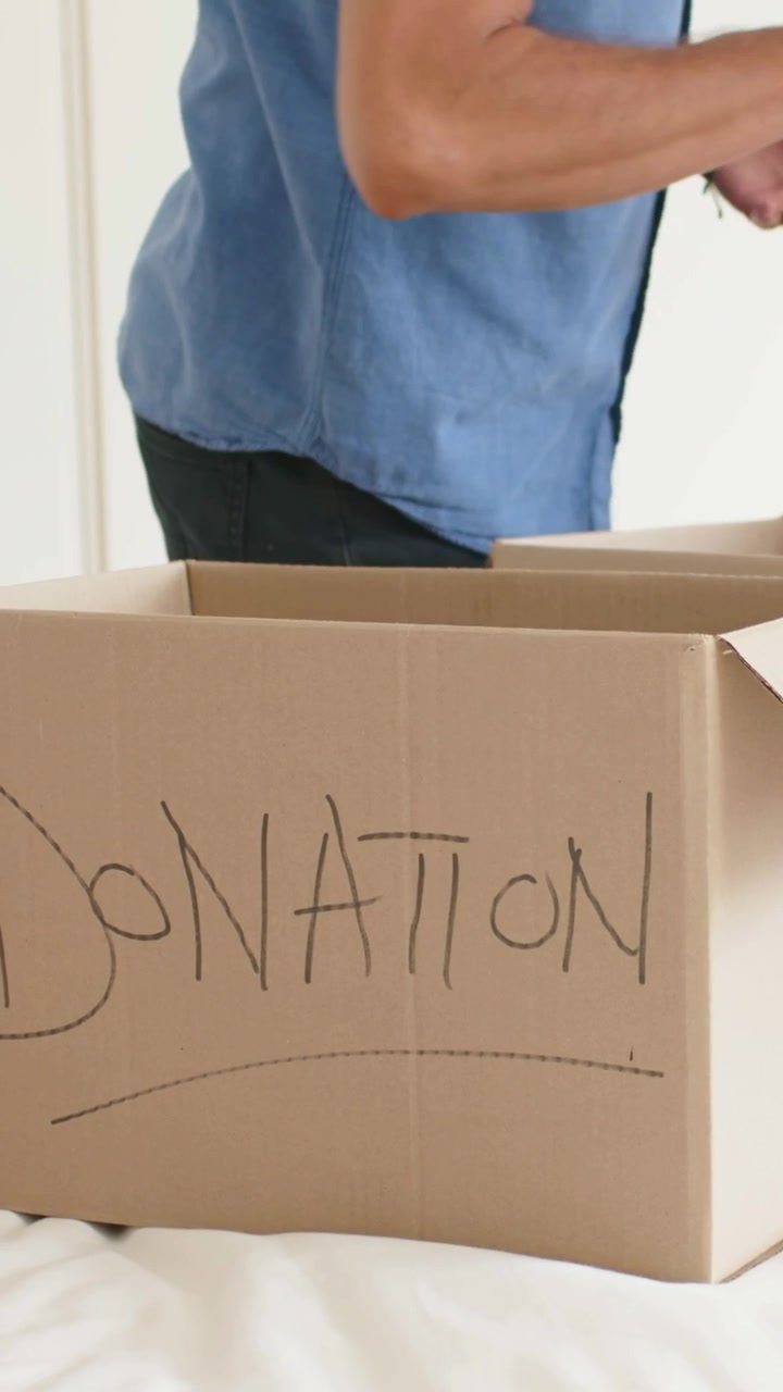 Vertical video: Inspecting shirt, mature man packing shirts into DONATION boxes at home for charity