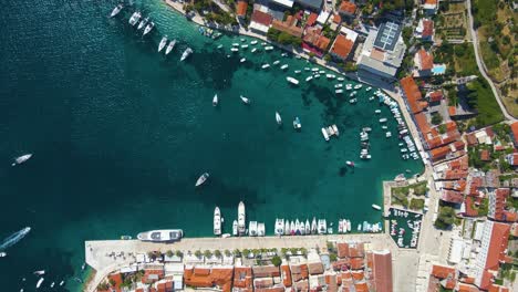 view of a coastal town with many houses with red roofs, surrounded by the sea and mountains with yachts in marina bay and bell tower
