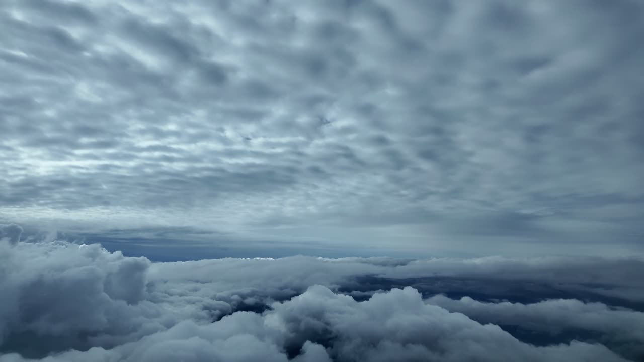 An airplane cockpit view while flying peacefully between layers of grey clouds in a dramatic sky