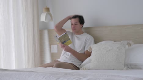 guy read book while sitting an leaning on the headboard of a bed